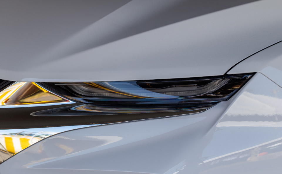Front corner and headlight of a silver car with a minor low-speed dent