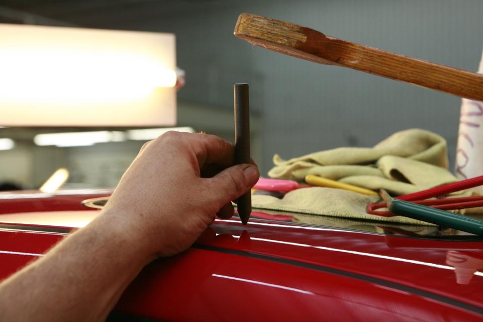 A technician working a dent out of a car panel by hand with paintless repair tools